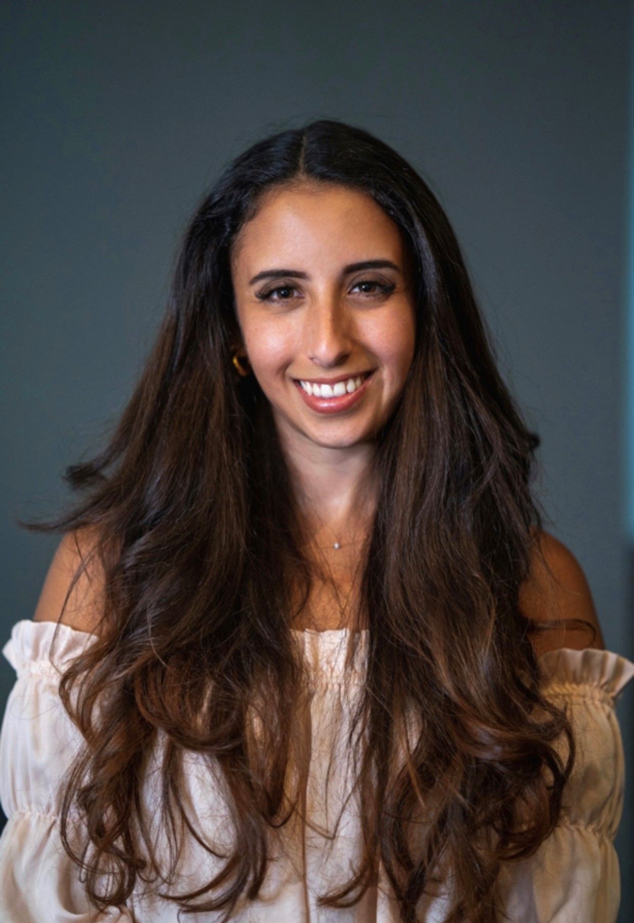 Person with long, dark wavy hair wearing a white off-shoulder top.